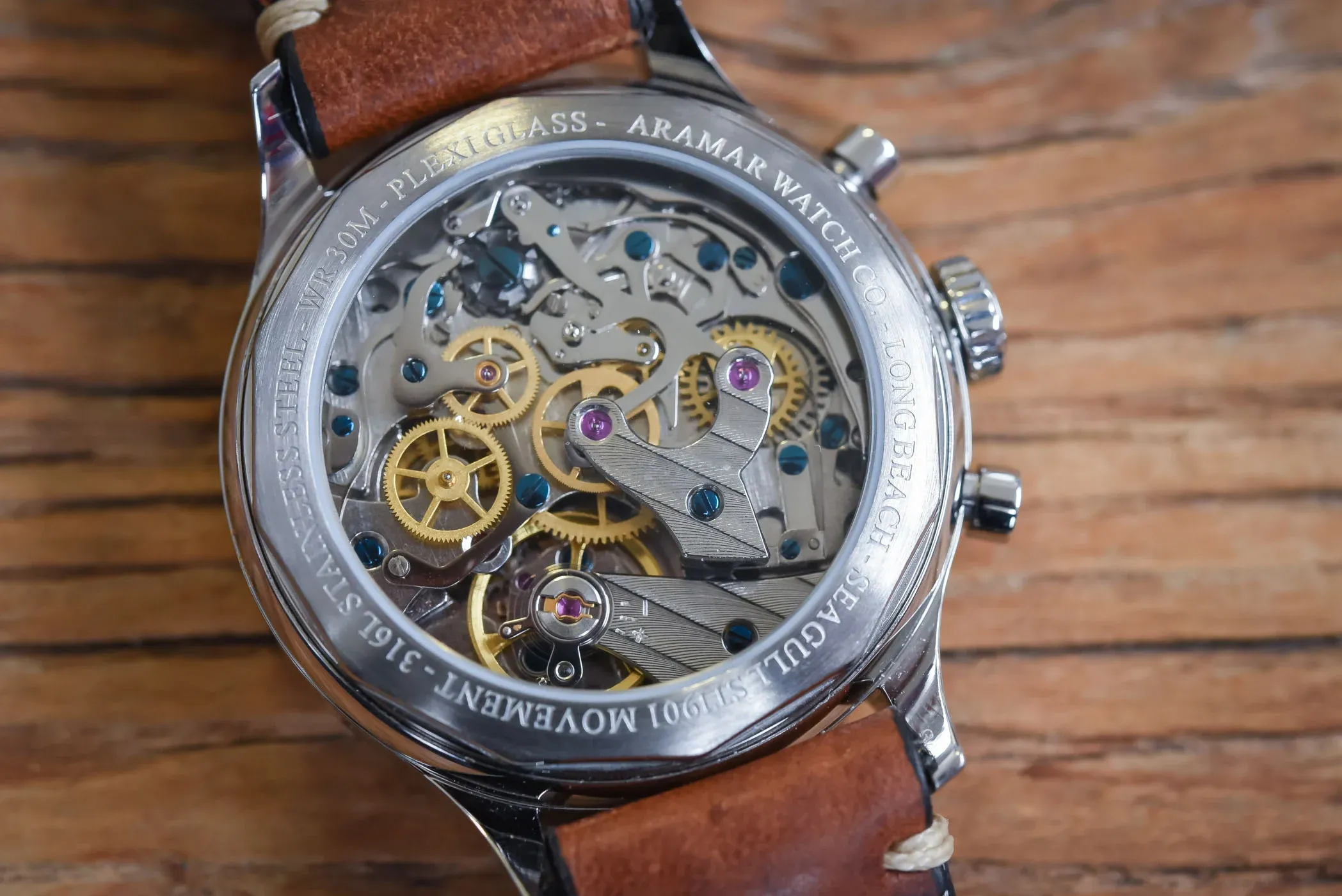 Open case back view of similar clone movement on wooden surface for power reserve demonstration.